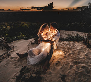 couple on a beach with lights around them at sun down